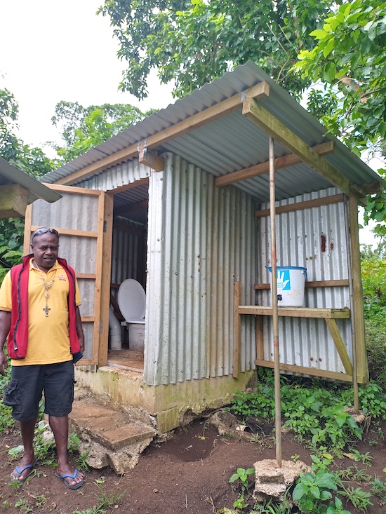 Fr Haggai in Tanbok community with a toilet that was built pre-COVID at the local pre-school. It has not only been renovated but a shelf has been added to hold a hand-washing bucket. © Terry Russell, AID.